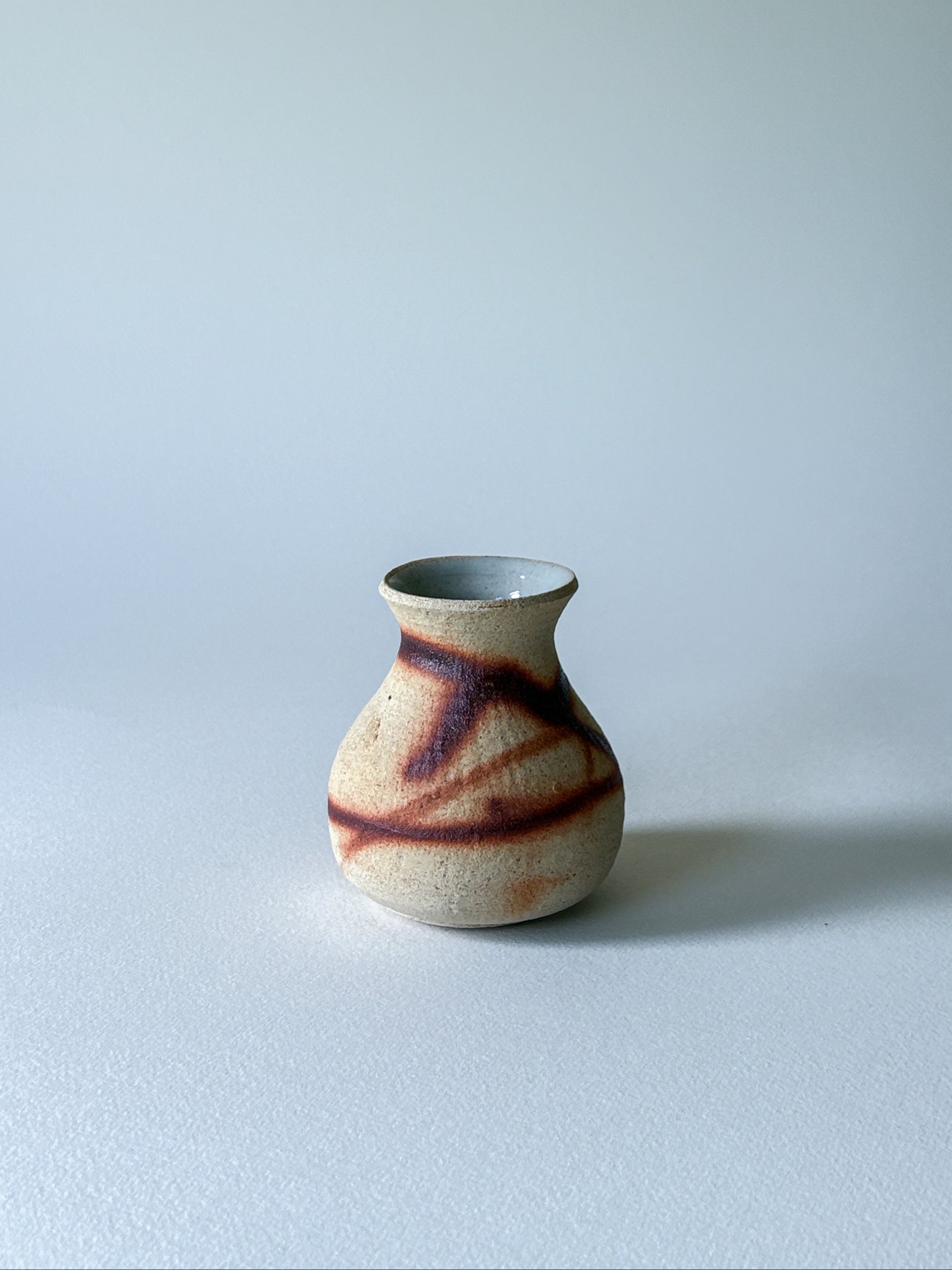Small ceramic vase with brown and beige patterns on a light gray background